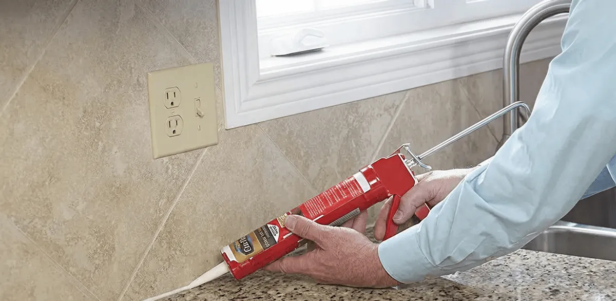 Handyman applying caulk along a kitchen backsplash and countertop seam in Fargo, ND