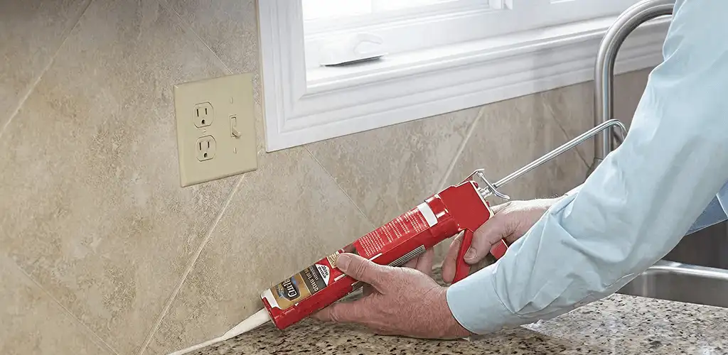 Handyman applying caulk along a kitchen backsplash and countertop seam in Fargo, ND